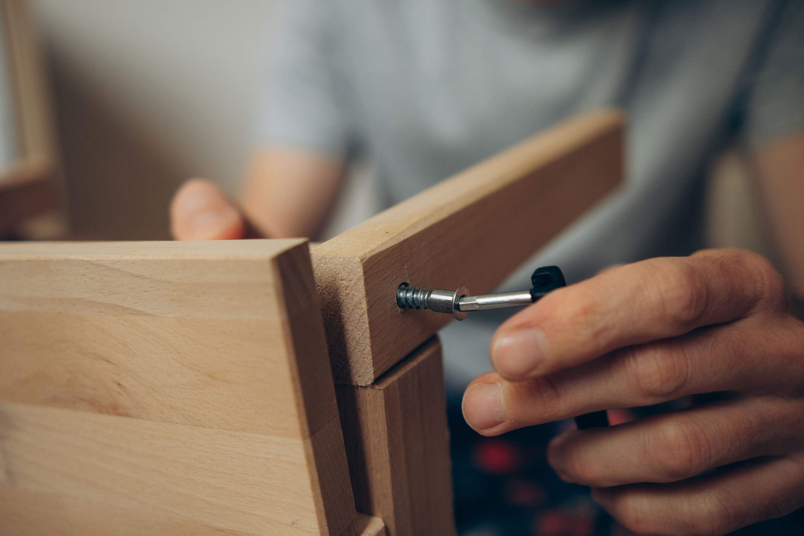 Hands assembling wooden panel components in workshop setting.